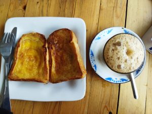 Roti Bakar Srikaya di atas piring putih dan di sebelahnya segelas teh tarik